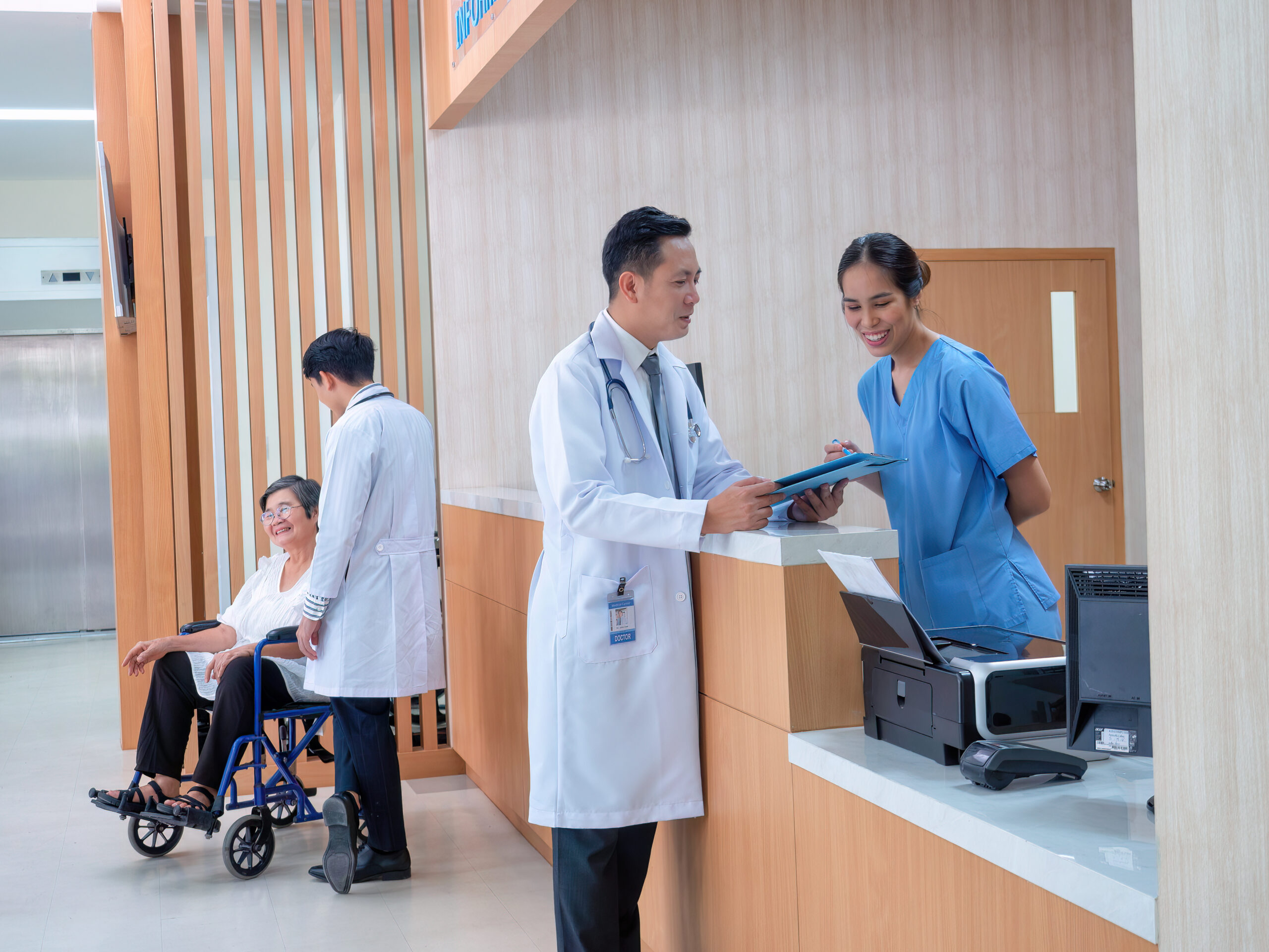 At hospital hall patient sit waiting information counter doctor speaking to administrative crew